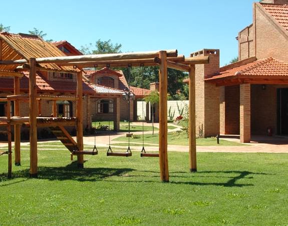 Cabañas de ladrillo visto con techos de teja y un juego de plaza sobre el césped en La Aldea Complejo