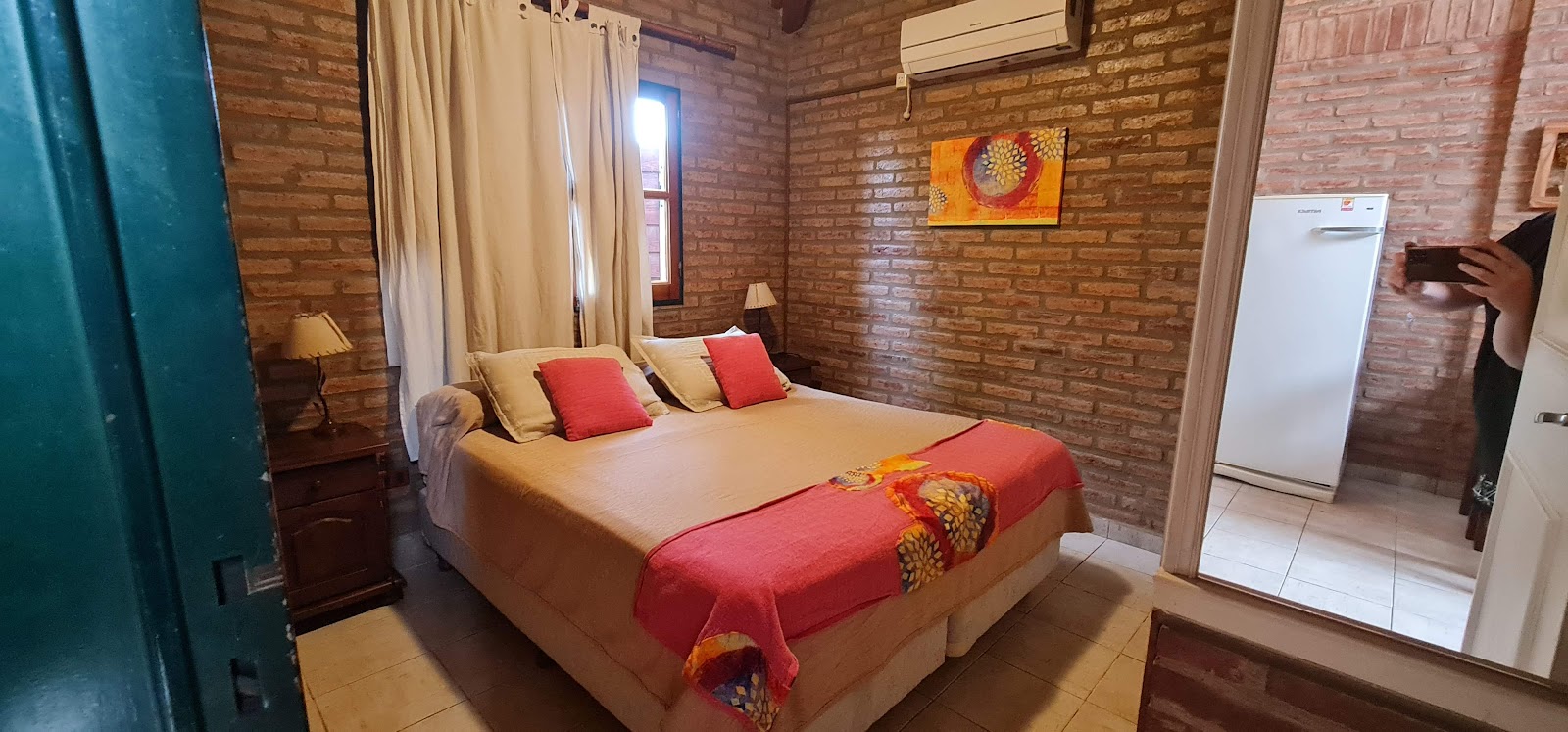 Dormitorio de cabaña con paredes de ladrillo visto, cama matrimonial, aire acondicionado y heladera